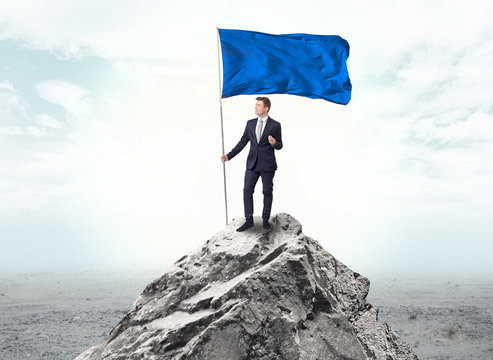 Handsome businessman on the top of the mountain with blue flag
