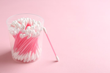 Plastic container with cotton swabs on color background. Space for text