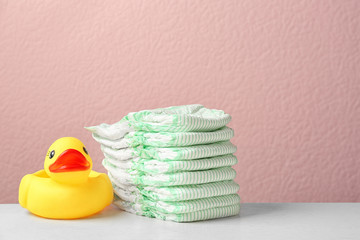 Stack of diapers and toy duck on table against color background, space for text. Baby accessories