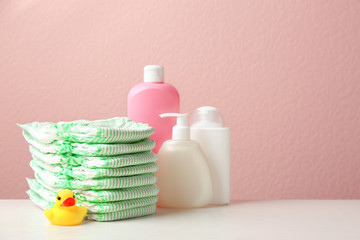 Stack of diapers, toiletries and toy duck on table against color background, space for text. Baby accessories