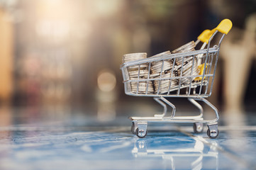 money coins in yellow shopping cart blur abstract background.