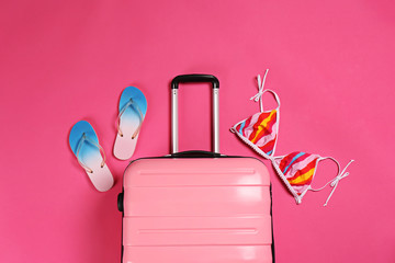 Stylish suitcase, bikini top and flip flops on color background, top view