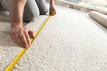 Man measuring carpet indoors, closeup view. Construction tool