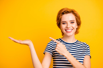 Close up photo beautiful amazing she her lady hold hand arm palm empty space point finger new product wear casual striped white blue t-shirt outfit clothes isolated yellow bright background