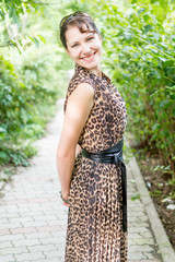 Portrait of happy and attractive young caucasian woman in nice dress in the summer park's alley. Beautiful natural green background.