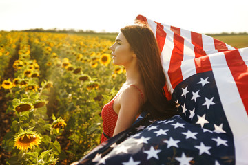 Beautiful girl with the American flag in a sunflower field. 4th of July. Fourth of July. Freedom....