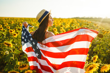 Beautiful girl in hat with the American flag in a sunflower field. 4th of July. Fourth of July....
