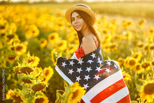 Beautiful girl in hat with the American flag in a sunflower field. 4th of July. Fourth of July. Freedom. Sunset light The girl smiles. Beautiful sunset. Independence Day. Patriotic holiday.