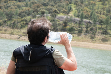 Hombre bebiendo agua de una botella con el fondo de un lago 