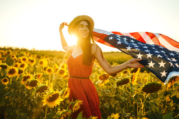 Beautiful girl in hat with the American flag in a sunflower field. 4th of July. Fourth of July....
