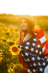 Fototapeta na wymiar Beautiful girl in hat with the American flag in a sunflower field. 4th of July. Fourth of July. Freedom. Sunset light The girl smiles. Beautiful sunset. Independence Day. Patriotic holiday. 