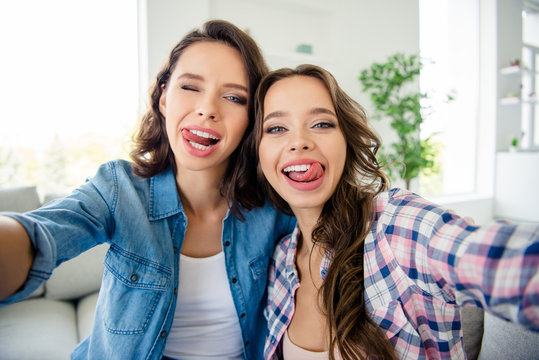 Close up photo beautiful she her cute ladies buddies meeting gathering make take selfies tongue out mouth wear casual jeans denim checkered plaid shirts apartments sit comfy divan couch room indoors