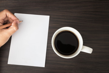 Left hand writing something on the paper and black coffee with copy space on dark brown table.