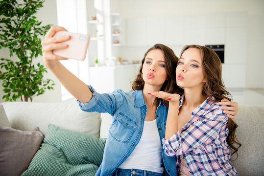 Close up photo beautiful amazing she her ladies buddies make take selfies telephone hand arm send air kiss coquette wear casual jeans denim checkered plaid shirts apartments sit divan couch indoors