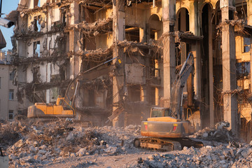 Fototapeta na wymiar Building demolition with hydraulic excavator. Dismantle of destructed house ruins at bright sunsest