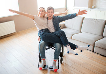 Young man with disability and inclusiveness holding girlfirend on knees. They smile and pose on...