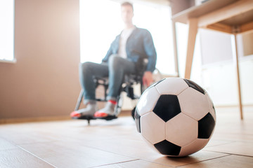Young man with disability sitting on wheelchair and look down at ball for game. Ex sportsman. Upset...