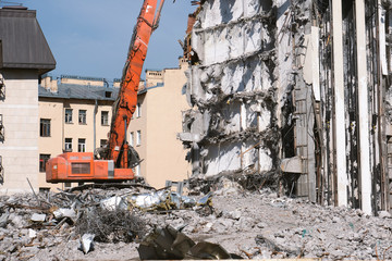 Building demolition with hydraulic excavator. Dismantle of destructed house ruins at bright sunny day with clear blue sky.