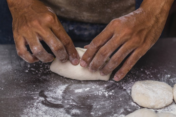 Male hands chef close-up, knead the dough, cook the dough on a dark background