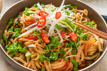Asian vegan lunch - spicy chow mein noodles with carrots, pepper and spinach with sliced radish, spring onions and chili peppers on a plate