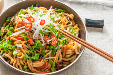 Asian vegan lunch - spicy chow mein noodles with carrots, pepper and spinach with sliced radish, spring onions and chili peppers on a plate