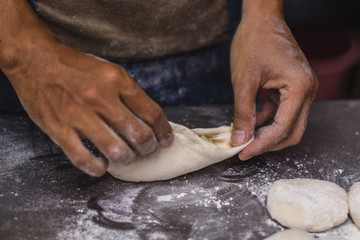 Male hands chef close-up, knead the dough, cook the dough on a dark background