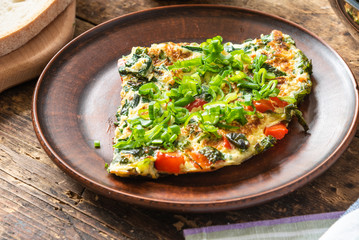 Home-made frittata with spinach and red pepper, sprinkled with spring onions on a plate and cutting board with bread, rustic style, close-up, top view