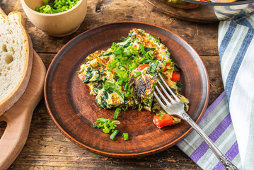 Home-made frittata with spinach and red pepper, sprinkled with spring onions on a plate and cutting board with bread, rustic style, close-up, top view