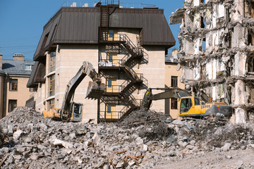 Building demolition with hydraulic excavator. Dismantle of destructed house ruins at bright sunny day with clear blue sky.