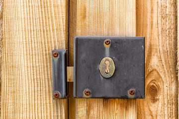 A weathered and worn metal lock mechanism with rusted screws on a wooden gate and fence post close up