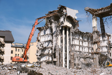 Building demolition with hydraulic excavator. Dismantle of destructed house ruins at bright sunny day with clear blue sky.