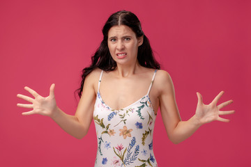 Fototapeta premium Portrait of a pretty young woman in a light dress standing on pink background in studio. People sincere emotions.