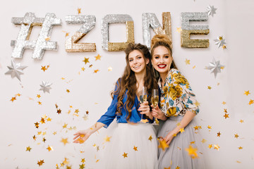 Happy party moments of attractive happy young women having fun in golden tinsels on white background with inscription Zone . Expressing true positive emotions, smiling, chilling, luxury lifestyle