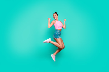 Fototapeta na wymiar Full length side profile body size photo beautiful she her funny stylish trendy hairdo jump high lucky lottery wear casual pink tank-top jeans denim shorts isolated teal turquoise background