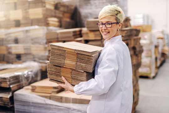 Smiling beautiful blonde woman relocating disassemble boxes in warehouse.