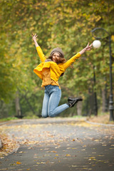 Happy Portrait fashion of a beautiful young Caucasian woman with a grey cap and scarf and yellow pullover in autumn park,red green yellow threes. Autumn, season and people concept.Autumn lifestyle