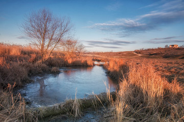 Spring morning on the river bank covered with a thin crust of ice. In the blue sky fluffy clouds. Rural landscape.