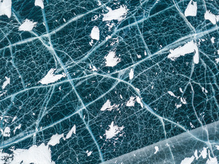 Top view of the network of cracks in thick solid layer of ice of a frozen Baikal lake in Siberia (Russia) from bird's eye. Icy landscape with rifts and snow, aerial shot.