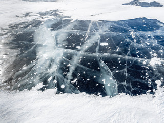 Network of cracks in thick solid layer of ice partially covered by snow of a frozen surface Baikal lake in Siberia (Russia)