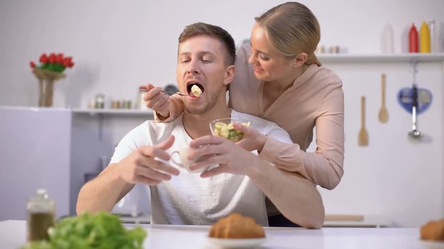 Lady playfully feeding husband with slice of banana, fruits as tasty vitamins