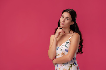 Portrait of a pretty young woman in a light dress standing on pink background in studio. People sincere emotions.