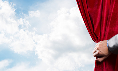 Cloudy landscape behind red curtain and hand holding it