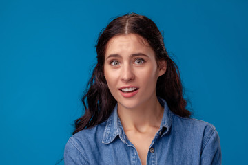 Close-up portrait of an attractive brunette girl with long curly hair posing on a blue background.