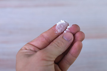 cocaine, heroin: a powdered narcotic drug on the tip of a man's finger, on a light background.