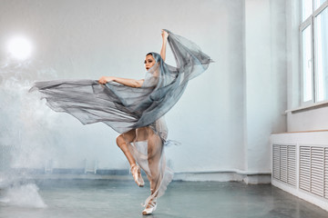 Full-size expressive photo of female ballet dancer dressed in grey-blue flowing fabric spinning on...