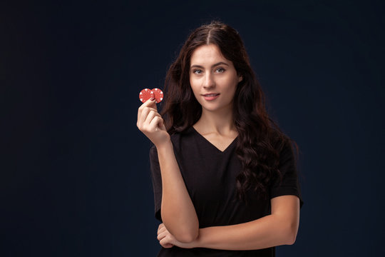 Curly hair brunette is posing with red gambling chips in her hands. Poker concept on a black background. Casino.