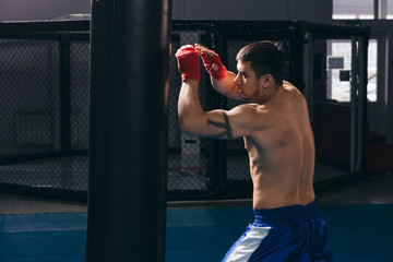 Young athletic man preparing for boxing competitions, training defense and attacks in fighting...