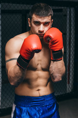 Young attractive shirtless man in boxing gloves posing in defense boxer stance isolated on dark background in sport and fitness exercise workout.