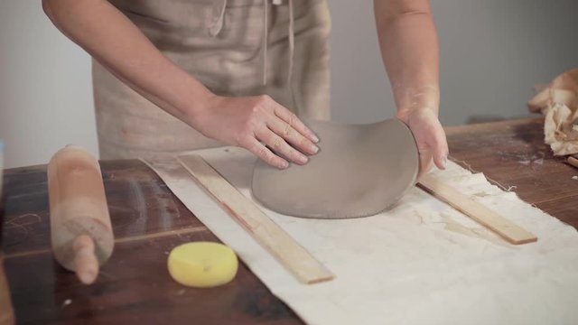 Artist is unrolling clay on table in workshop, using pin, close-up of hands