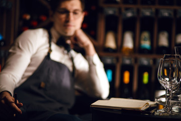 Portrait of sommelier perfectly skilled in wine etiquette, selecting wines, exquisite service for presenting wine to the customer putting down some notes in his note pad in restaurant.